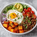 Sweet potato ground beef bowl topped with avocado, fresh herbs, and seasoned beef.